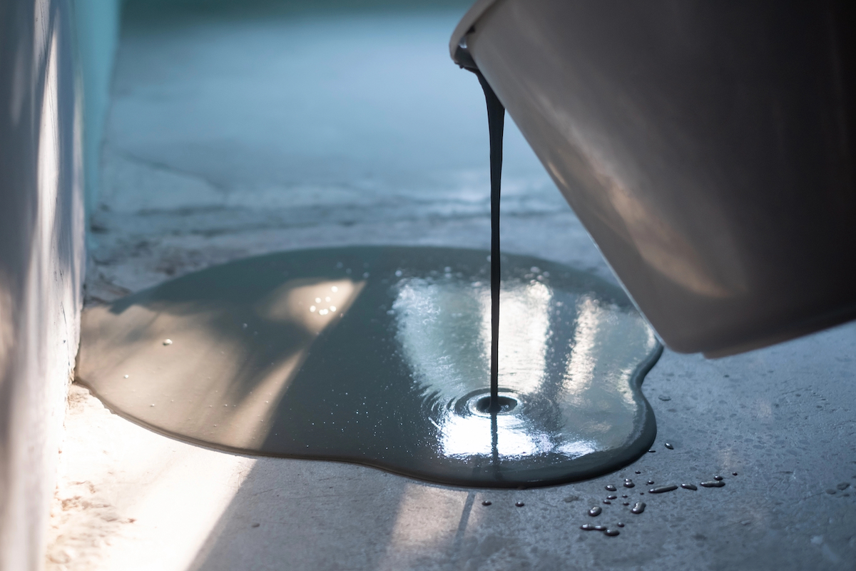 Pouring self-leveling compound from a black bucket onto a concrete floor.